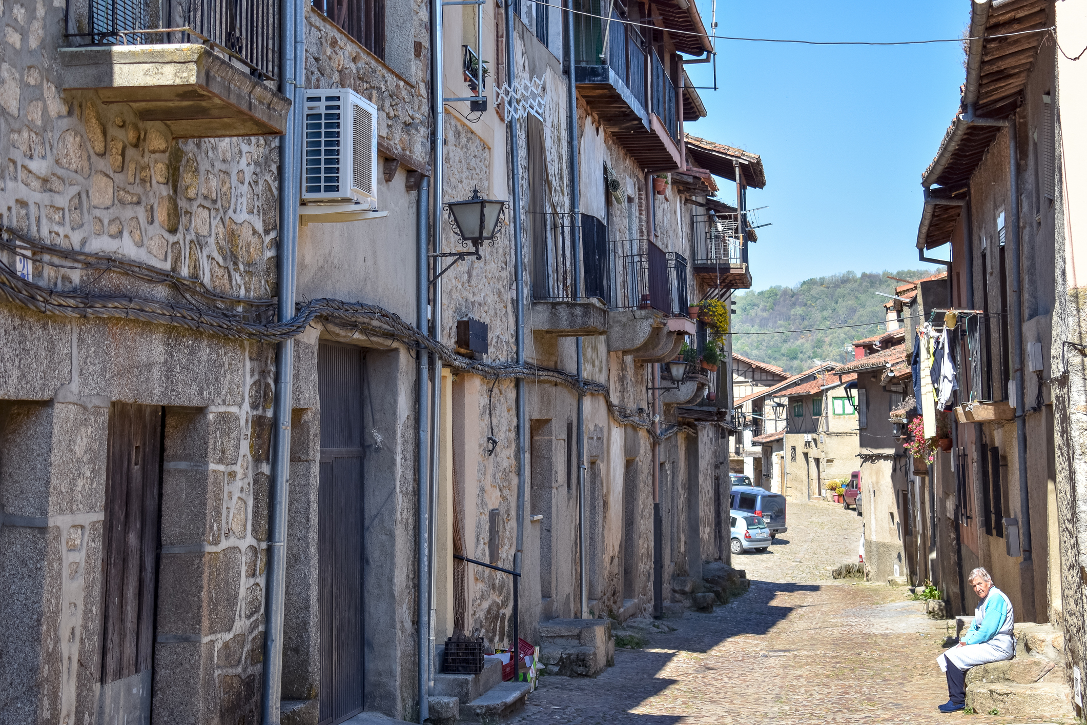 An old woman alone sitting on a bench enjoys a sunny day on an empty street. It reflects the depopulation of rural areas in Spain due to lack of employment.